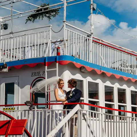 Couple in wedding attire on a boat deck under a blue sky.
