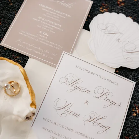 Wedding invitations with rings and orchids on a dark surface.