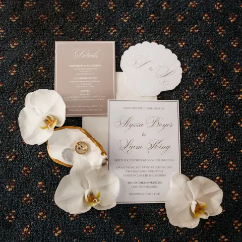 Wedding invitations on carpet with white orchids and seashells.