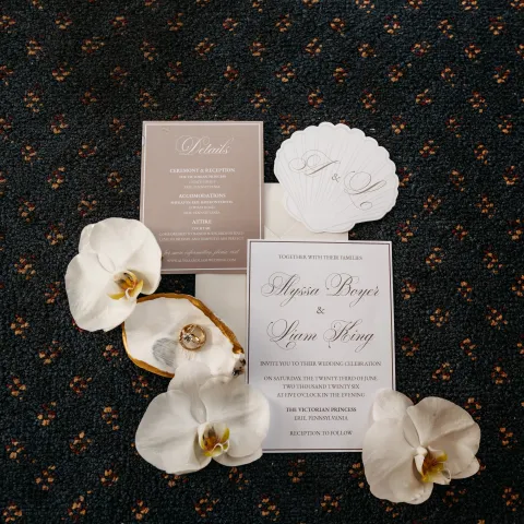 Wedding invitations and orchids on a patterned blue carpet.
