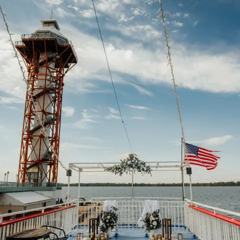 Deck with chairs and U.S. flag overlooking water and red tower under cloudy sky.