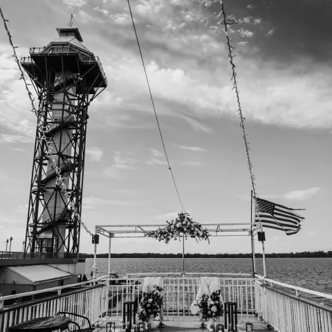 Black and white view from a ship deck with an American flag and a tall tower in the background.