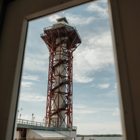 Red steel observation tower viewed through a window with a blue sky.