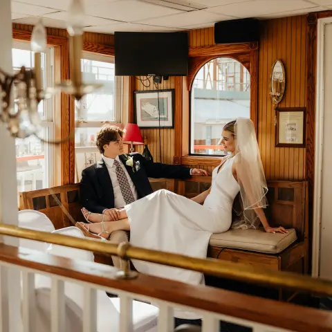 Bride and groom sitting on a boat, with elegant decor and large windows.