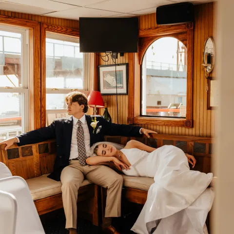 Couple in wedding attire relaxing on a boat, bride resting on groom's lap.