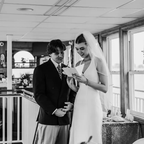 Bride and groom reading a letter together indoors, in black and white.