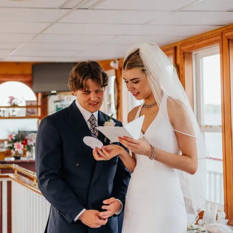 Bride and groom reading a card indoors, with windows in the background.