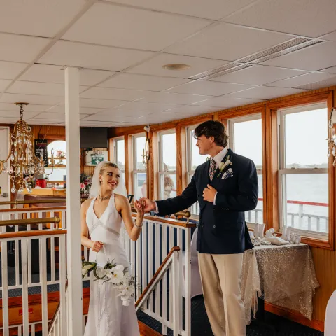 Bride and groom on a boat staircase, holding hands, with a banquet table nearby.