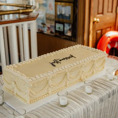 Rectangular cake with beige icing, small candles surrounding, and a wood-paneled wall in the background.