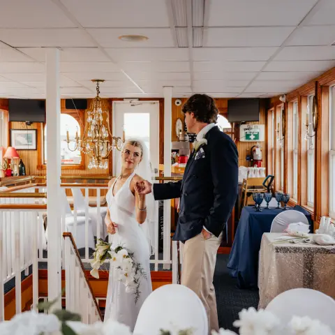 Bride and groom on a decorated boat interior, holding hands and looking at each other.