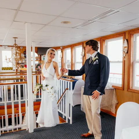 Bride and groom on a boat, holding hands, in formal attire.