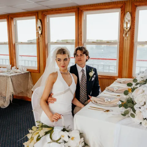 Bride and groom seated at a table with flowers in a bright room.