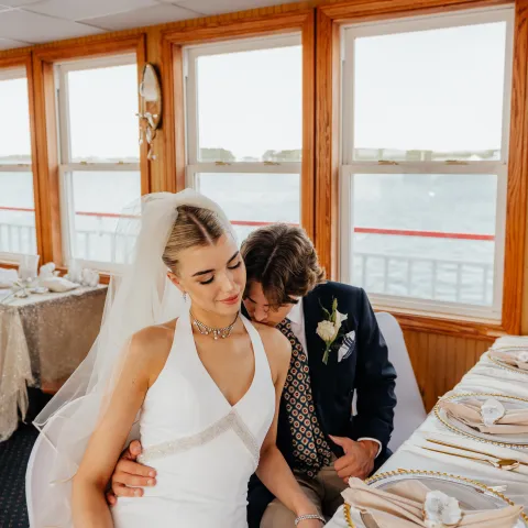 Bride and groom sitting at a table on a boat with a view of the water.