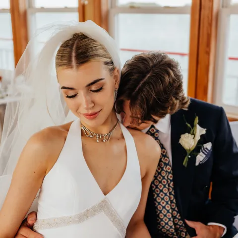 Bride in white dress with veil sits with groom in dark suit and tie.