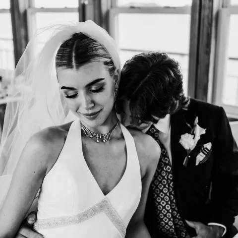 Bride in white dress with veil, groom in suit sitting closely, black and white photo.