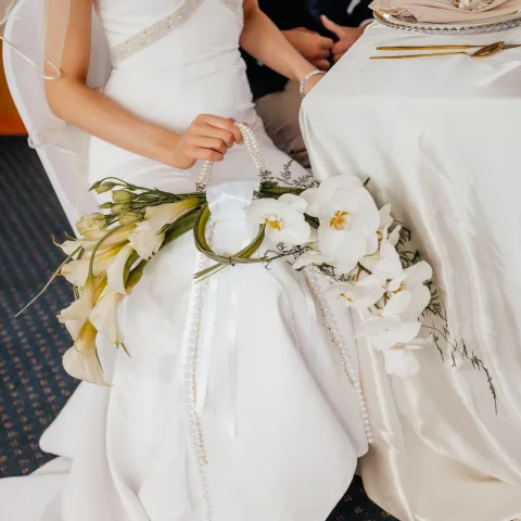 Bride holding bouquet with white flowers, seated at a table.