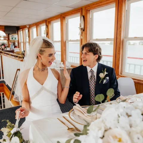 Bride and groom smiling at each other seated at a table with floral decorations.