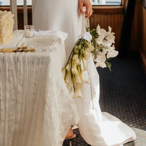Bride in white holding bouquet, standing by a decorated table.