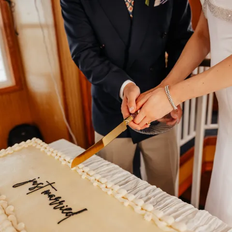 Couple cutting rectangular wedding cake with 'just married' on top.