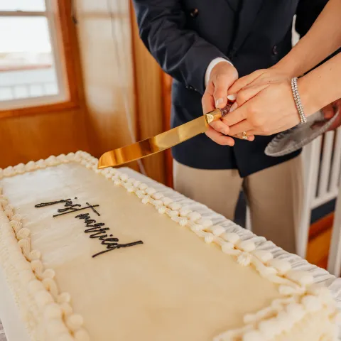 Couple cutting a rectangular 'just married' cake on a table.