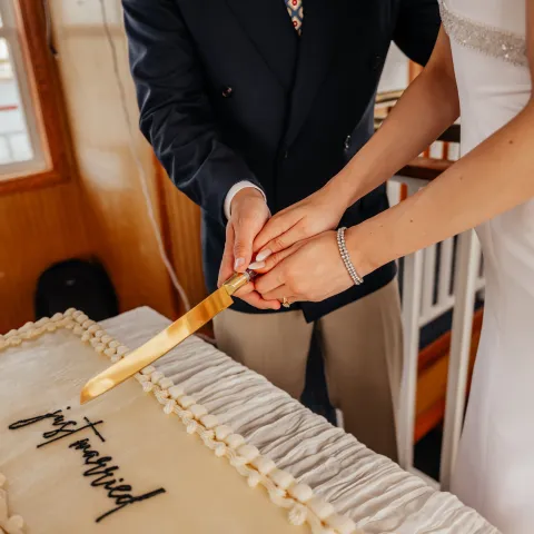 Couple cutting a rectangular wedding cake together with a golden knife.