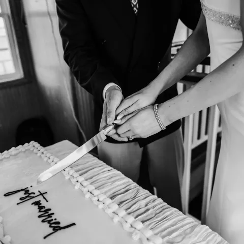 Bride and groom cutting a rectangular wedding cake together.