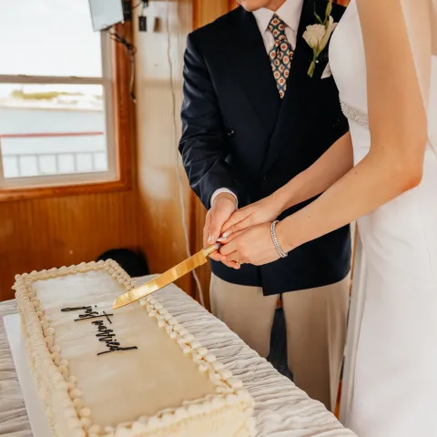 Couple cutting a white rectangular wedding cake together indoors.