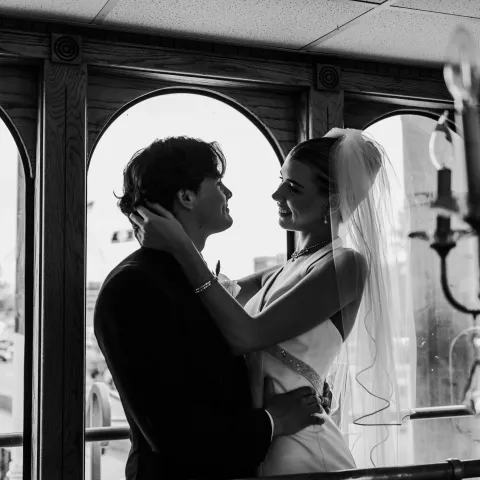 Bride and groom embracing near large windows, black and white photo.
