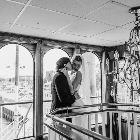 Black and white photo of a couple embracing by a window on a boat.