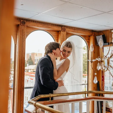 Bride and groom embracing on a staircase inside a wooden building.