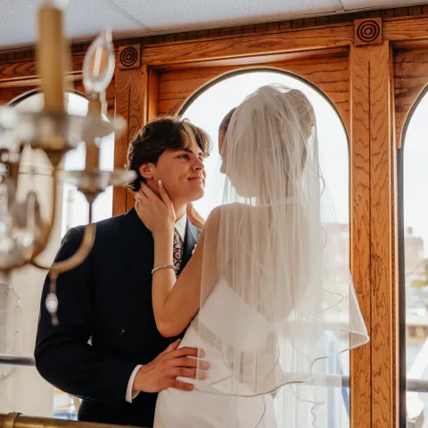 Bride and groom embrace on a balcony, wooden window backdrop.