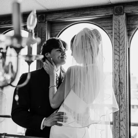 Bride and groom gaze at each other in a venue with arched windows.