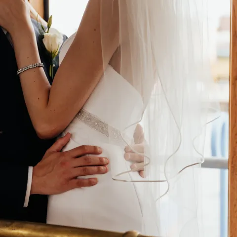 Bride and groom embracing near a railing with a white veil.
