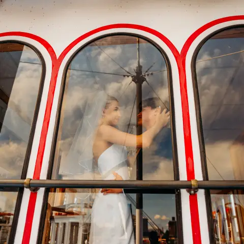 Bride and groom embracing behind arched windows with reflections.