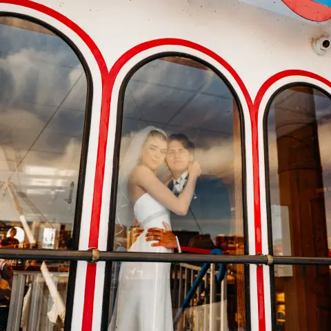 Bride and groom embrace behind arched windows on a boat with 'Princess' sign.