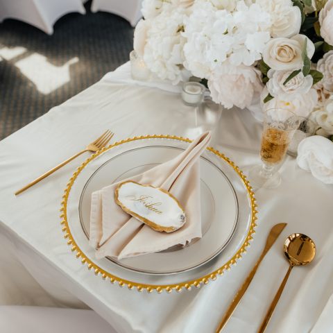 Elegant table setting with flowers, gold cutlery, and a plate with a napkin and name card.