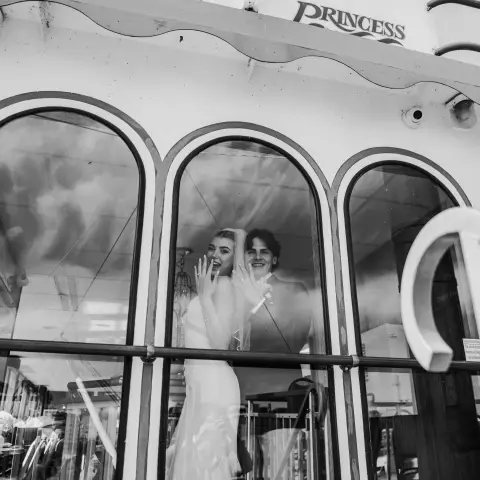 Bride and groom wave from a boat named 'Victorian Princess' through large windows.