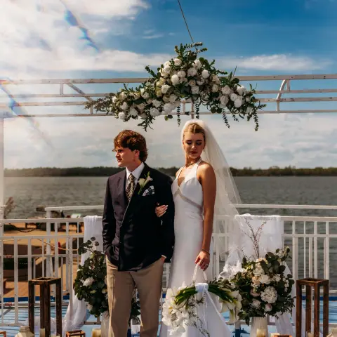 Bride and groom posing on a decorated outdoor platform by the water.