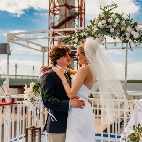 Bride and groom embracing on a boat deck with floral arch.