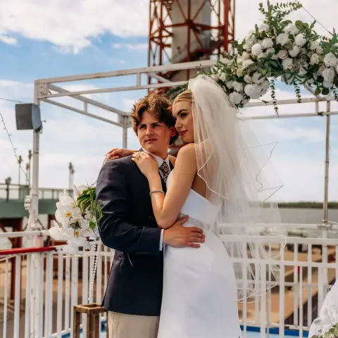 Couple posing at an outdoor wedding ceremony with floral arch.