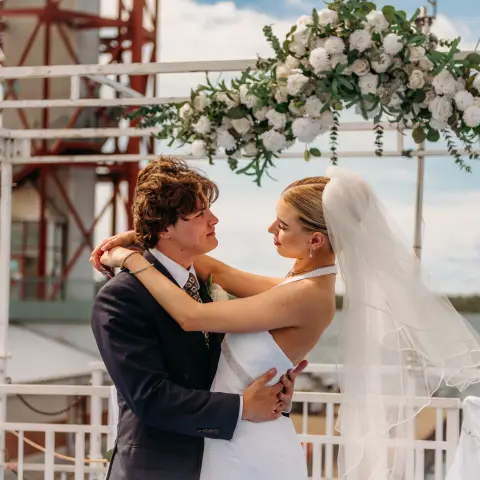 Bride and groom embracing under floral arch outdoors.