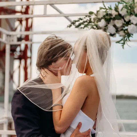 Bride and groom kissing under an arch by the water.