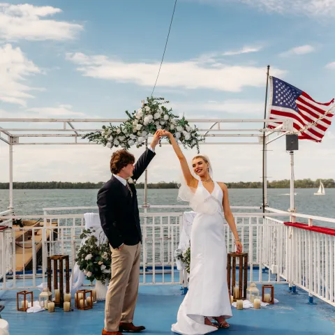 Couple dancing on a boat deck with ocean and flag backdrop.