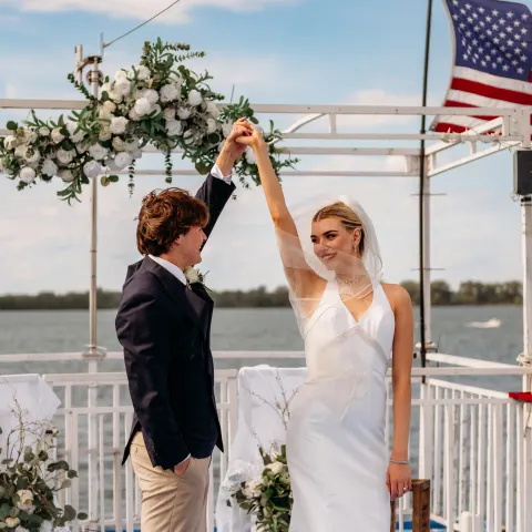 Bride and groom dancing on a decorated deck by a lake with an American flag.